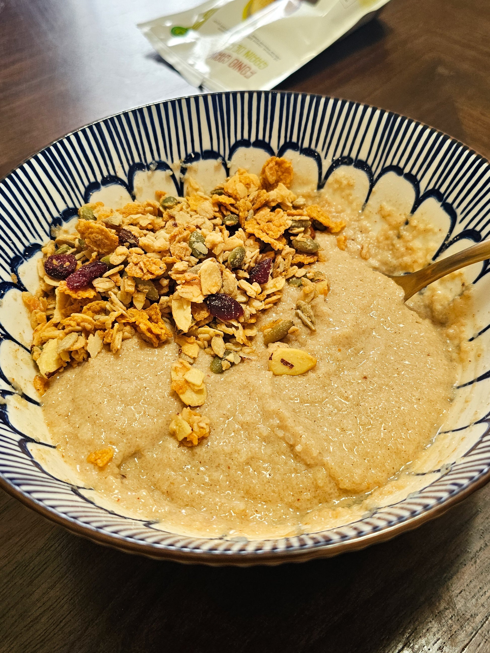 Bowl of fonio pudding with granola and dried fruits on a wooden table